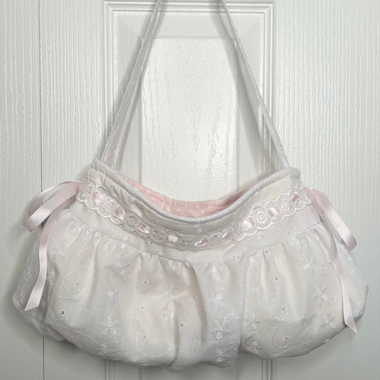 Light gray bag with pink ribbons on a white wooden background